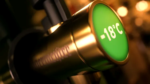 A close-up of a metallic cylindrical tap with a glowing green circular end marked '-18°C' in white text, photographed in warm, low-light conditions.