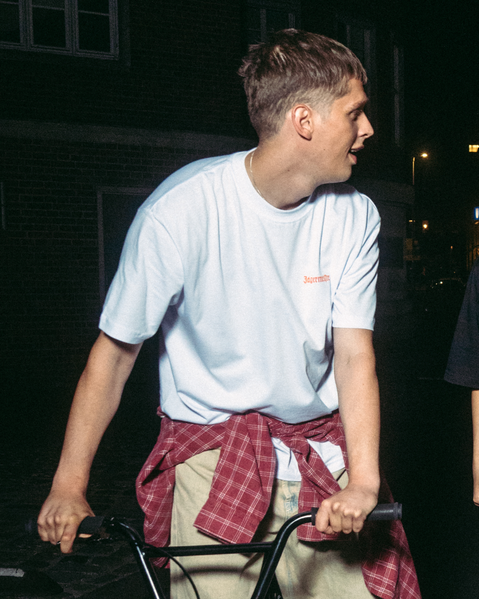 Persona in bicicletta di notte, con addosso una maglietta bianca Jägermeister con un piccolo logo sul petto.