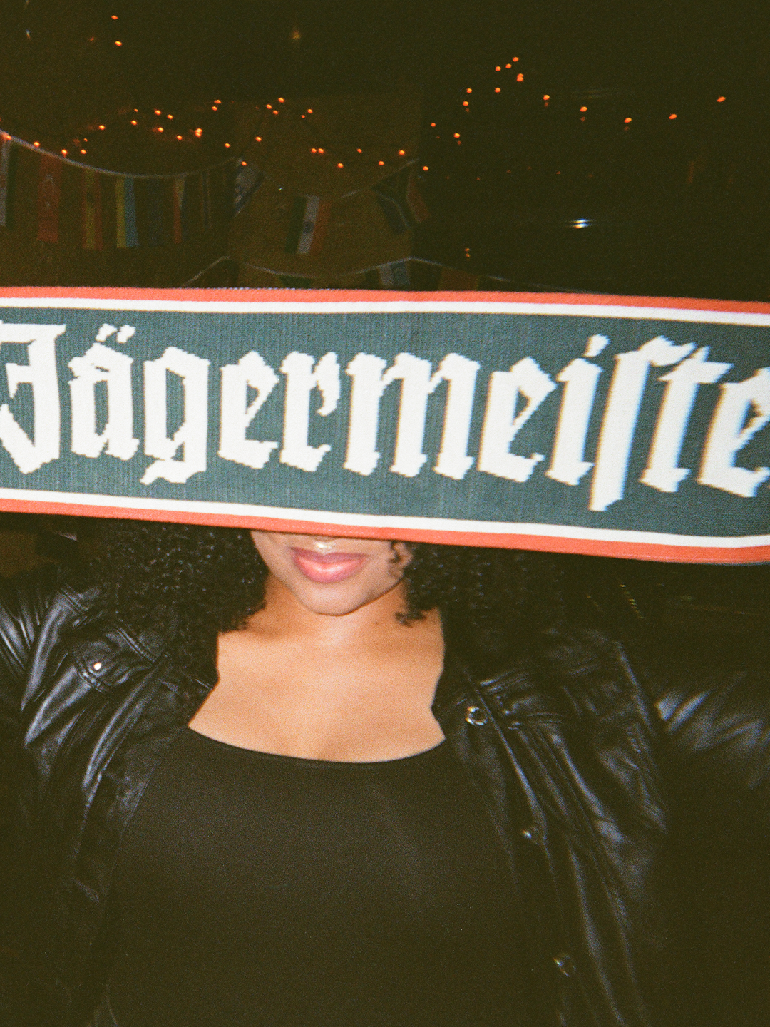 Persona che tiene una sciarpa Jägermeister davanti al viso con uno sfondo scuro.