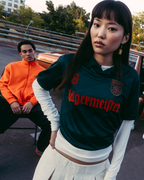 Un gruppo di quattro persone posa all’aperto davanti a un’auto d’epoca marrone. La figura centrale indossa una jersey Jägermeister verde scuro, mentre le altre sono vestite con streetwear casual.