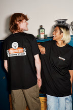 Due persone che indossano t-shirt nere da corsa Jägermeister con un logo e del testo, in piedi vicine l’una all’altra.