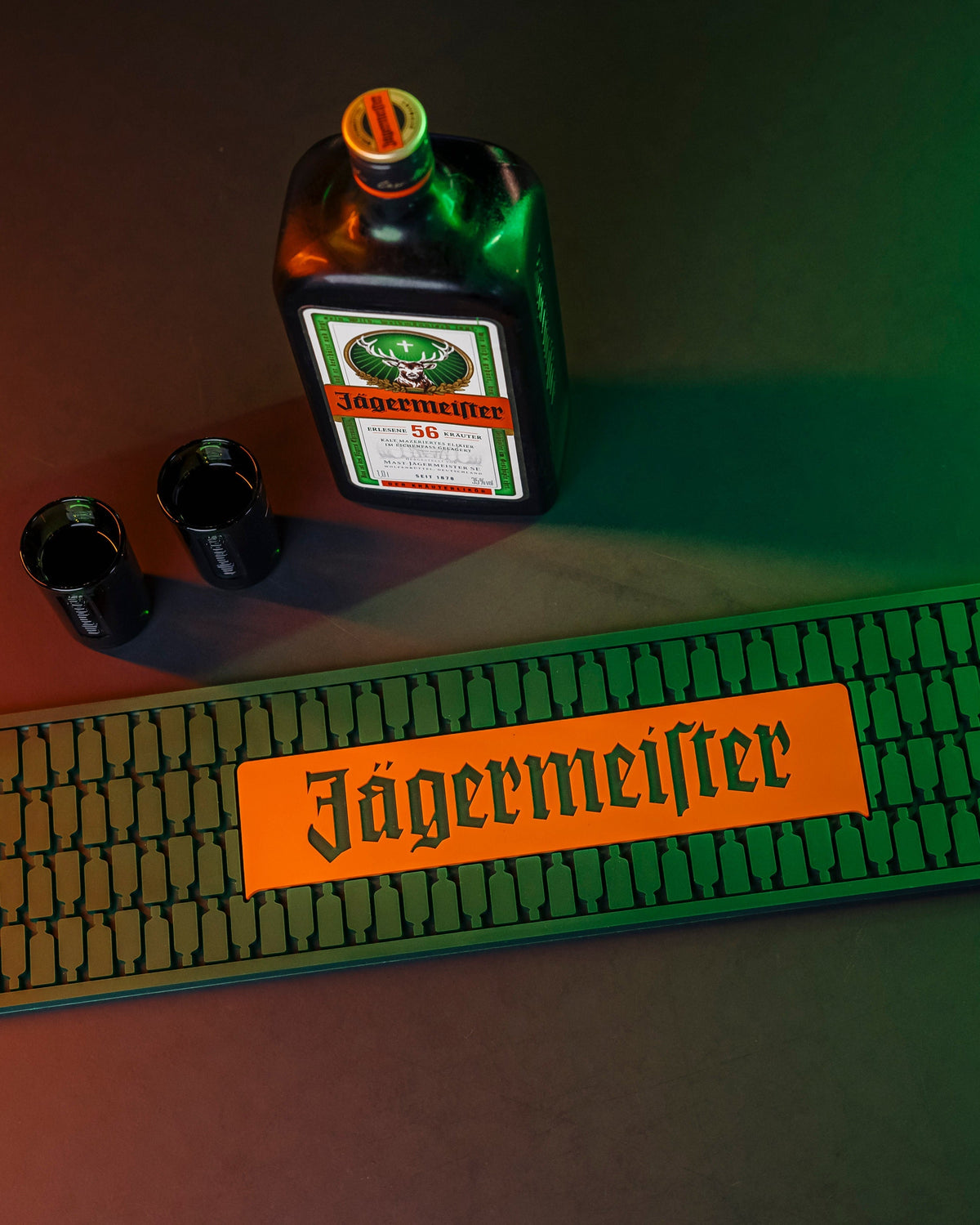 Bottiglia Jägermeister, due shot glass e bar mat su una superficie scura
