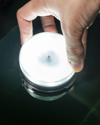 Mano che tiene una piccola fonte luminosa rotonda su una superficie scura