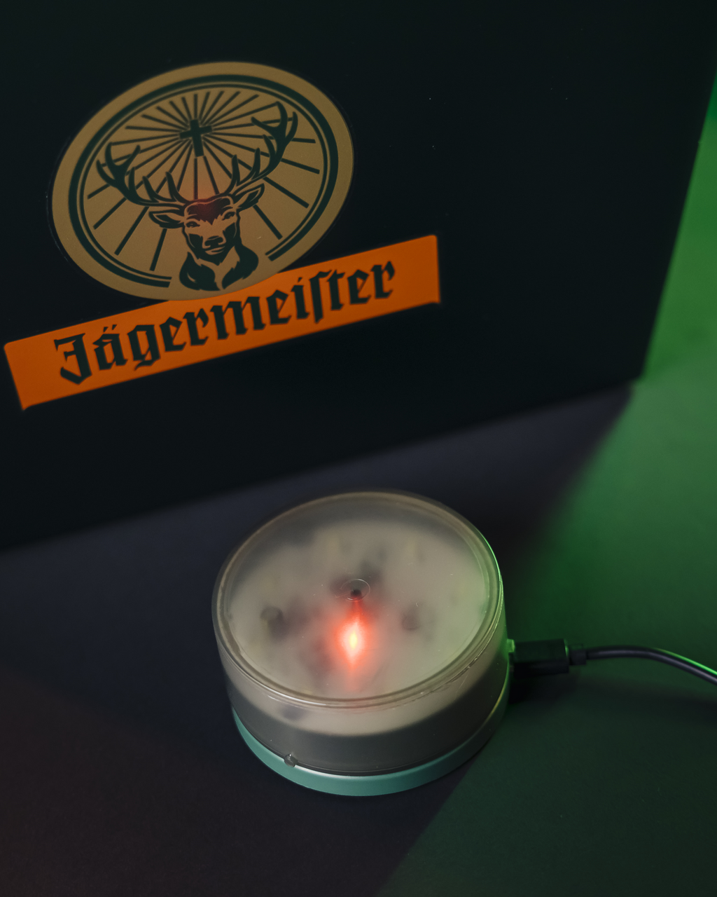 Logo Jägermeister su sfondo scuro con un piccolo dispositivo rotondo che emette luce.