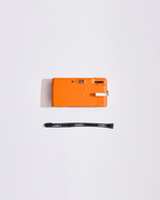 Fotocamera arancione con tracolla su sfondo bianco