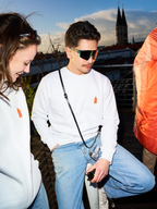 Due persone con felpe bianche Jägermeister e occhiali rapidi Jägermeister su una terrazza panoramica, con un campanile e lo skyline della città sullo sfondo.