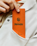Jägermeister e Kuumba su carta profumata arancione tenuta in mano contro uno sfondo di camice bianco