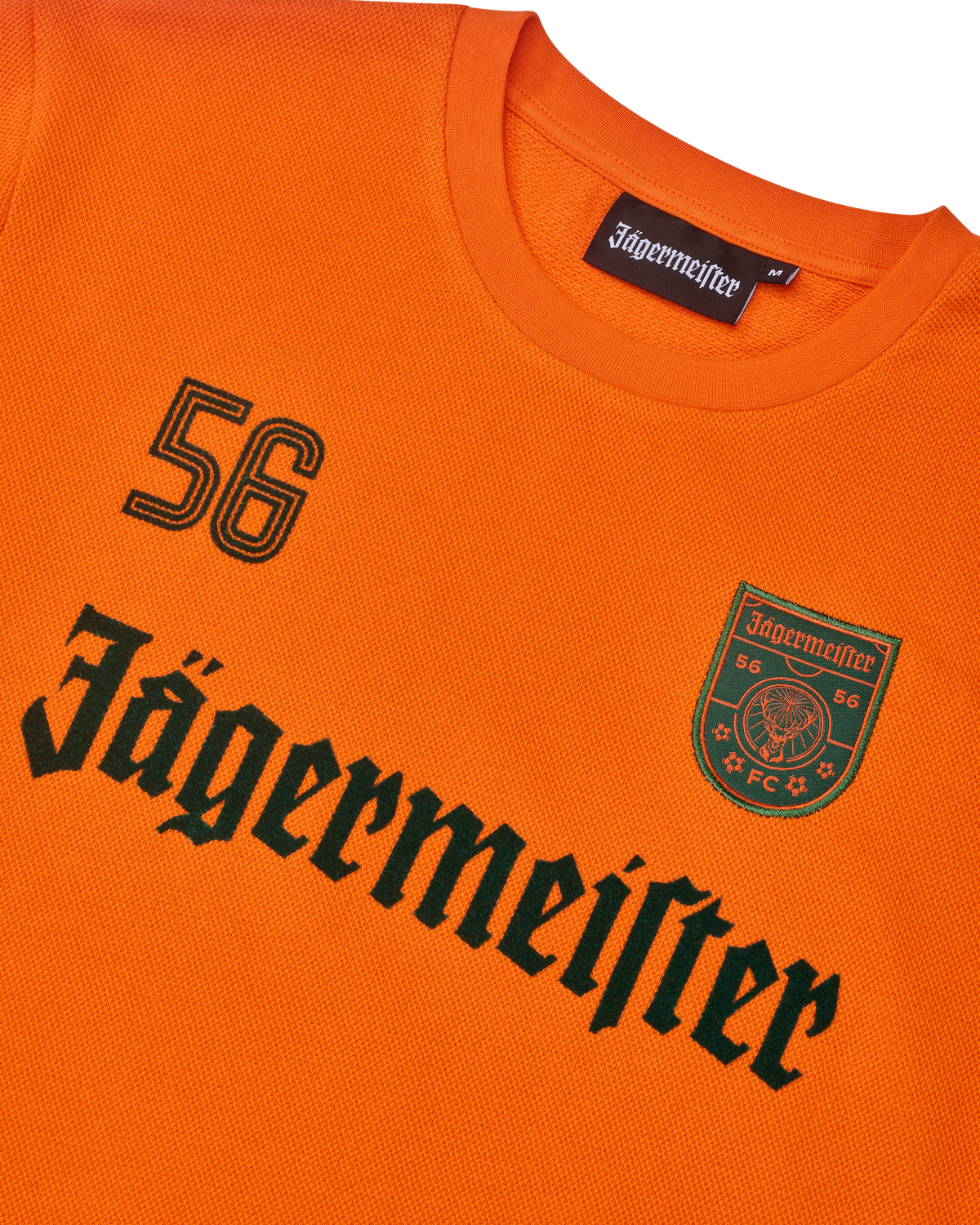 Maglia a maniche lunghe arancione Jägermeister con scritta Jägermeister nera e un '56'.