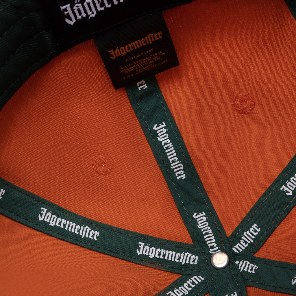 Cappellino arancione Jägermeister Racing con branding Jägermeister sulla fascetta e sulla sua etichetta.