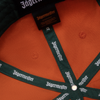 Cappellino arancione Jägermeister Racing con branding Jägermeister sulla fascetta e sulla sua etichetta.