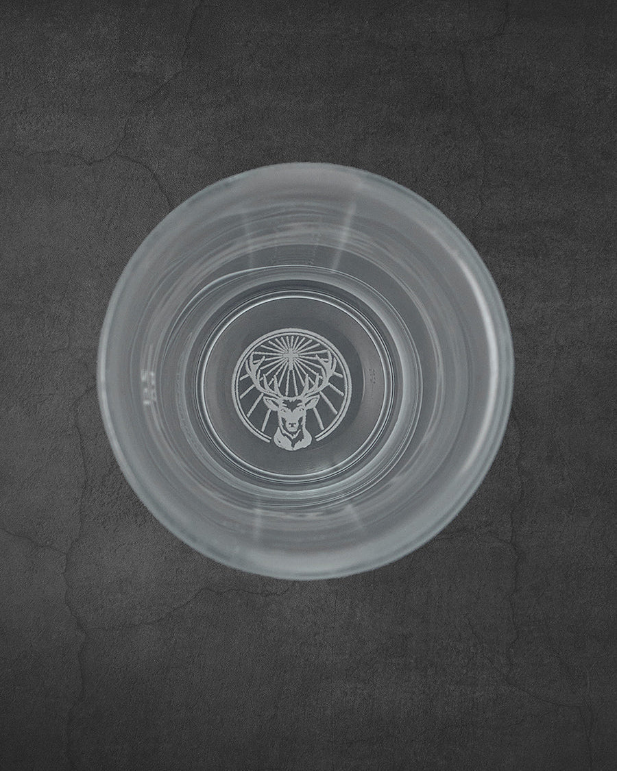 Bicchiere shot Jägermeister bianco visto dall’alto con logo del cervo sul fondo
