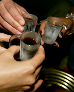 Quattro mani che tengono bicchieri shot Jägermeister satinati, pieni di un liquido scuro, mentre brindano.