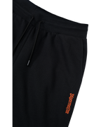 Pantaloni della tuta neri con logo Jägermeister arancione sul lato.